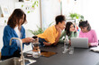 © Studio Marmellata - Four diverse young women gather in a modern kitchen. One prepares pour-over coffee while three friends collaborate on a laptop at the counter. They share a casual moment.