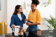 © Studio Marmellata - Two diverse young women are in a modern kitchen. One shows content on her smartphone to the other, who holds a kettle. They are preparing pour-over coffee and sharing a moment.