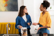 © Studio Marmellata - Two young women are in a modern kitchen. One holds a kettle while the other shows content on her smartphone. They share a friendly conversation.