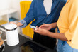 © Studio Marmellata - Two individuals are in a modern kitchen. One person holds a white electric kettle, while the other operates a smartphone. They are preparing a hot beverage together.