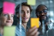 © ttonaorh - Group of young professionals collaborating during brainstorming session, using colorful sticky notes on glass wall in modern office.