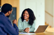 © bnenin - African-American Woman Laughing During Friendly Job Interview At Table With Laptop In Modern Office