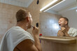 © Sarolta Nagy - Rear view of a man shaving his face with a razor while looking into the bathroom mirror.