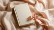 © Pavel - Elegant cream colored book resting gently on soft beige fabric with a delicate ribbon bookmark to enhance its charm and appeal at a cozy reading nook
