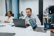 © qunica.com - A modern office scene with colleagues at a white table. A man types on a laptop while others review documents and collaborate in the background, illustrating focus and productivity.
