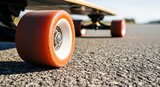 Longboard with vibrant orange wheels rests on a textured asphalt surface, showcasing the smooth ride and dynamic cruising experience in an outdoor setting