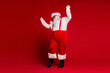 © deagreez - Santa Claus in red suit with suspenders dancing in a bold red studio for festive season and holiday magic