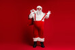 © deagreez - Santa in red suit with bag and suspenders stands against red background ready for holiday fun and festive shopping mood