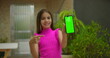 © Marco - Young girl smiling and pointing at smartphone with green screen and chroma key, highlighting customizable display in a vibrant outdoor setting