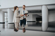 © qunica.com - Two courteous professionals in light suits converse in a bright, modern lobby. A tablet is shared as they discuss plans, presenting a confident, collaborative business moment.