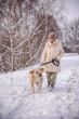 © StockMediaSeller - Elderly woman walking her Golden Retriever along a snow-covered path in the countryside. The woman holds the leash and smiles warmly at her dog during a quiet winter stroll among bare trees.
