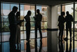 © qunica.com - Silhouetted coworkers converse in a glass-walled atrium, reviewing notes and notes of documents. A moment of collaboration and teamwork in a contemporary corporate environment.