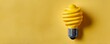 © PLOYCRAMER - Vibrant Spiral Yellow Light Bulb Against Textured Yellow Background Symbolizing Energy and Creativity