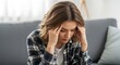 © MdLutfur - Worried woman with a headache sitting on a couch, depicting stress, anxiety, and mental health concerns, with a blurred background suggesting a home setting
