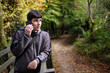 © Мар'ян Філь - A young man in a grey hoodie talks on a mobile phone while leaning on a wooden railing along leaf-covered forest path. Young man has negative emotions, dissatisfaction, anxiety while talking