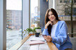 © insta_photos - Young smiling happy woman business lady or student sitting in city cafe holding smartphone device using mobile cell phone and laptop technology, working or learning online and looking at camera.