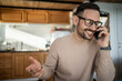 © Migma_Agency - Young man making phone call smiling in kitchen
