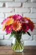 © Maryna - Colorful gerbera daisies in glass vase on wood table. White brick wall background. Fresh floral arrangement brightens room decor. Spring summer bouquet.
