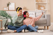 © Pixel-Shot - Happy brother and sister in headphones sitting on floor and taking selfie in living room