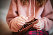 © Chatchaa - Woman hands opening an empty wallet. A close-up of a person wearing a pink sweater, holding an open wallet, possibly checking for money or cards, while sitting comfortably.