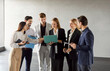 © Studio Romantic - Group of company employees discussing work project on laptop standing in office during a meeting. Confident young business people looking on computer monitor screen in conference room.