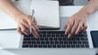 © tippapatt - Close up of business woman using laptop, searching the information and writing on notebook, business planning. Student studying online class via laptop, e-learning, online research