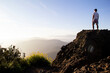 © Cavan Images - Man on rocky summit gazing at sunlit misty mountain landscape