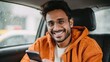 © LimeSky - Smiling young Indian man in casual attire and glasses sits in a taxi using his smartphone to chat with friends