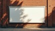 © Vadym - Large blank white horizontal billboard on old red brick wall building with concrete sidewalk. Sunny day casts tree leaf shadows across empty outdoor advertising space frame. Public urban street area