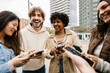 © Xavier Lorenzo - Happy young group of diverse friends having fun using mobile phones at city street, texting messages or watching social media content on cell app