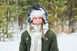 © pressmaster - Portrait of Caucasian teenager boy smiling into camera with face and winter hat covered in snow standing outdoors in snowy forest during cold weather