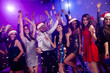 © deagreez - Fun party crowd celebrates together dancing at a neon lit club Christmas party with Santa hats and confetti