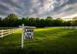© Asad - Land for sale sign on a wooden post in front of a vast green pasture with a white fence, under a dramatic cloudy sky during a beautiful sunrise