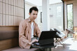 © Natthawadee - Young man working on his laptop in a modern cafe, focused and relaxed in a bright, natural-light workspace.
