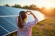 © Pete - Young girl shows heart sign near solar panels at sunset. Child loves clean solar energy and renewable power. Future generation cares for eco power.