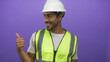 © Krakenimages.com - Young hispanic man wearing white hardhat and yellow reflective safety vest giving thumbs up gesture in purple studio; confidence motivation optimism success.