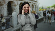 © Krakenimages.com - Woman smiling with glasses in front of the coliseum in rome surrounded by people and ancient architecture on a sunny day, showcasing joyful travel vibes.