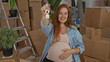 © Krakenimages.com - Pregnant woman holds house keys forward while cradling her bare belly in a modern home interior with moving boxes; anticipation.