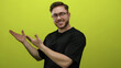 © Krakenimages.com - Young man with a beard in glasses presenting with open hands against a bright yellow background looks cheerful and engaging, ideal for business or creative presentations.