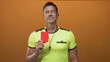 © Krakenimages.com - Referee man holds red card close to chest with eyes closed in orange studio wearing yellow referee shirt and whistle; calm judgment.