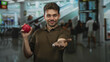 © Krakenimages.com - Man offers red apple with outstretched hand inside train station building, smiling with closed eyes and visible forearm; generosity welcome.