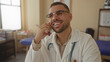 © Krakenimages.com - Young hispanic man holds smartphone with both hands and smiles in clinic; professional communication.