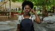 © Krakenimages.com - Woman wearing apron touches head while standing on city street with blurred trees and people in outdoor urban setting, showcasing thoughtful expression in casual attire.
