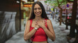 © Krakenimages.com - Woman touching hands to chest in red crop top on a busy urban street with trees and storefronts; gratitude.