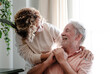 © luciano - Elderly man smiling warmly holding hands of a caregiver woman indoors. The scene captures tenderness, affection, and emotional connection, symbolizing affection, care, and companionship in later life