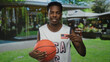 © Krakenimages.com - Young african american man in usa basketball jersey holds basketball and points finger to flag patch in street; patriotism.