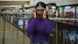 © Krakenimages.com - Woman wearing purple top adjusting eyeglasses with both hands by railing in mall indoors; confidence poise.
