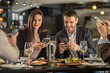© Creative Light - Friends enjoying a meal at a restaurant while using their smartphones