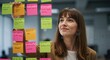 © NN AI - Creative professional woman brainstorming ideas with colorful sticky notes on glass board. Businesswoman working on project management and strategic planning in modern office