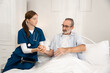 © Thitiporn - Home care nurse giving medication and water to elderly man in bedroom. Professional caregiver assisting senior patient with daily medical needs in a comfortable and supportive home environment.